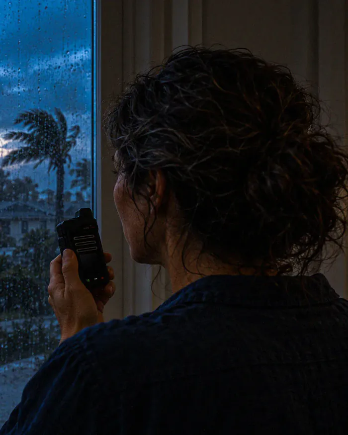 A woman at a rain-streaked window during a storm, speaking into a radio